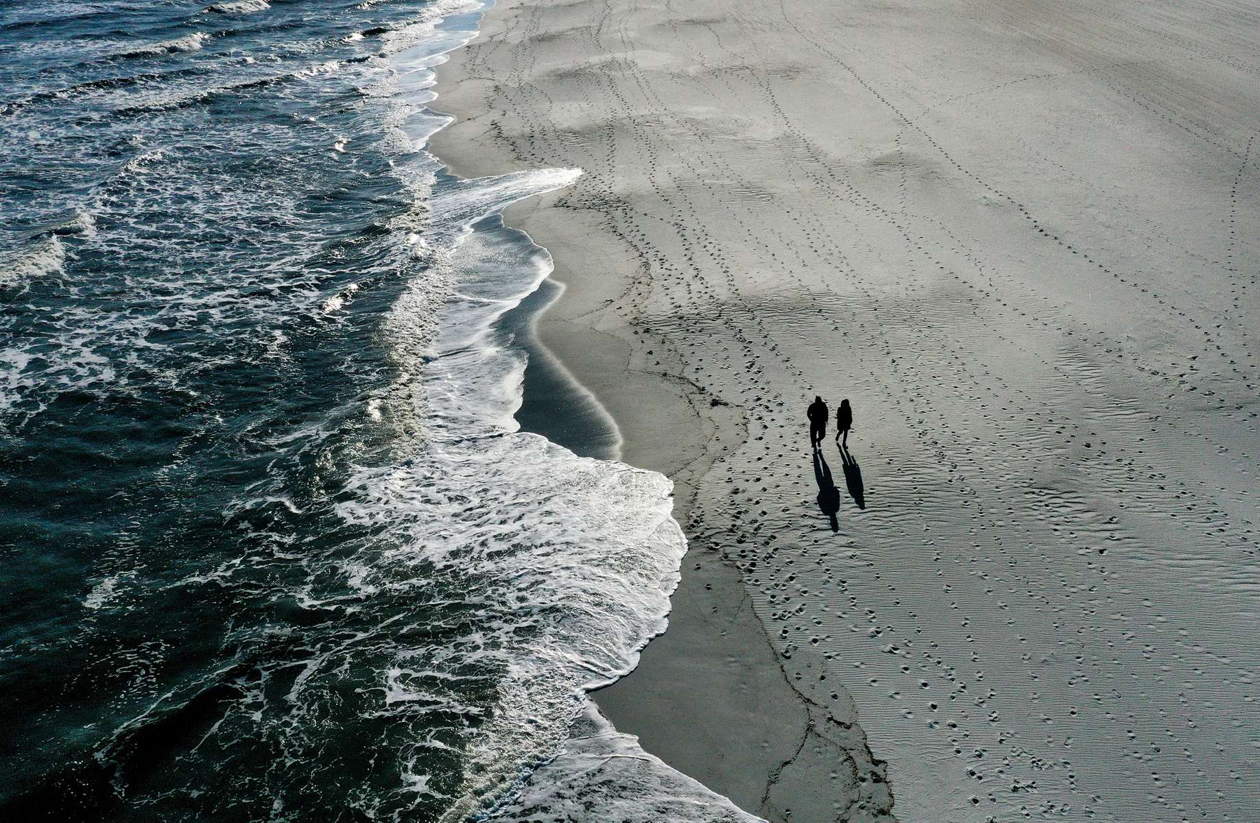 An aerial view of a couple walking on the sand by the ocean of Long Beach on April 22, 2020 in Long Beach, New York.  The boardwalk has remained closed since March 27 due to the coronavirus COVID-19 pandemic.The World Health Organization declared coronavirus (COVID-19) a global pandemic on March 11th.  