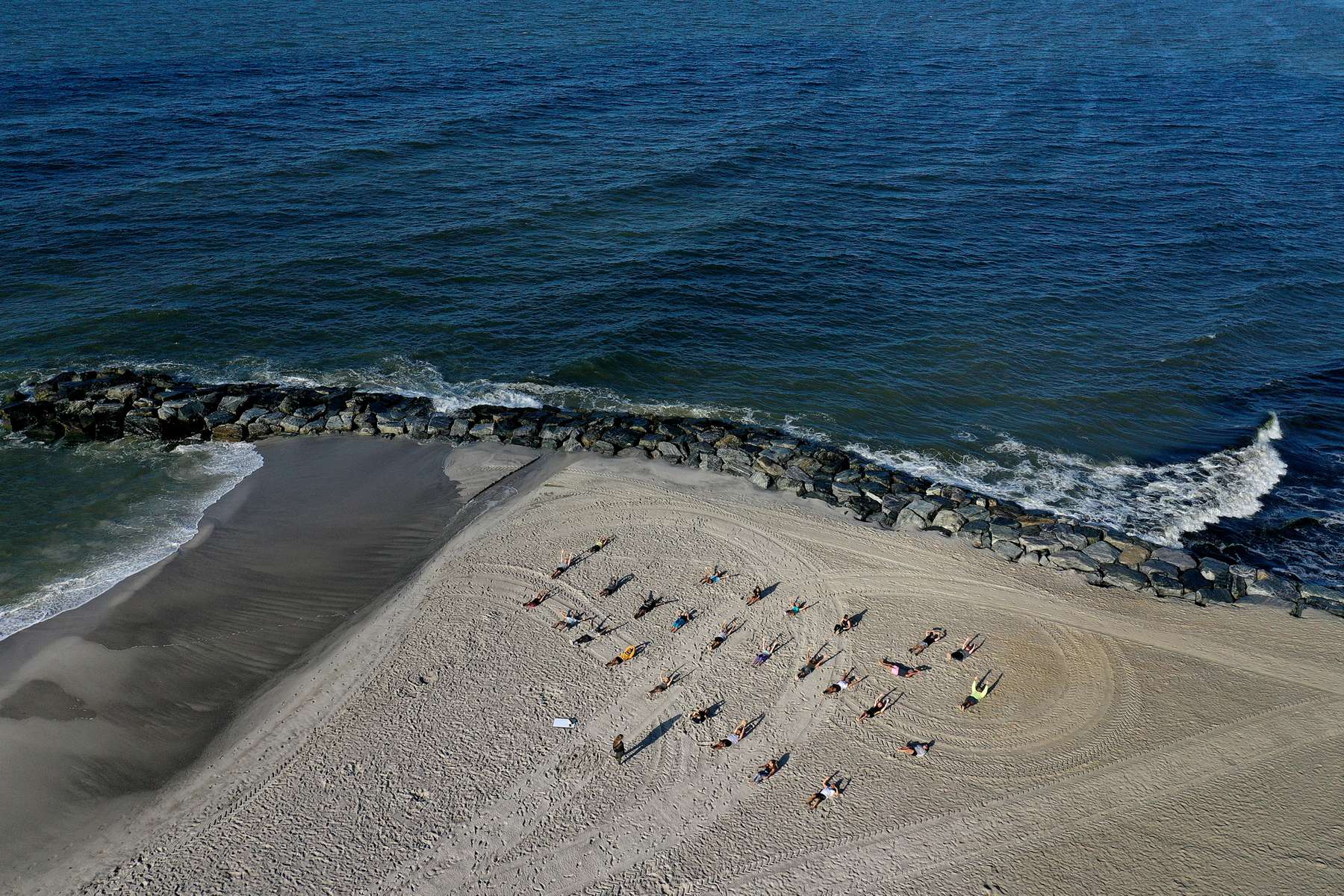 An aerial view of members of the {quote}Life Outside The Box {quote} Fitness Club during a training session led by fitness instructor Alexa Hoovis at the beach on August 18, 2020 in Long Beach, New York.  Gyms, which have been closed in New York since mid-March to help prevent the spread of the coronavirus, will be allowed to open again as soon as August 24th Governor Andrew Cuomo has announced.  Gyms will be limited to a third of their capacity, and they need to maintain a sign-in sheet to help contact tracers in case of a virus outbreak. Air filters must be able to help prevent the transmission of viral particles. People must wear masks at all times. 
