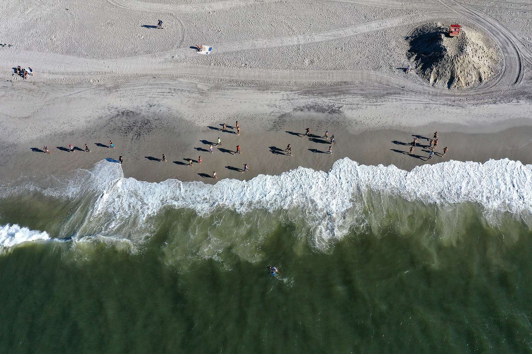 An aerial view of members of the {quote}Life Outside The Box {quote} Fitness Club during a training session led by fitness instructor Alexa Hoovis at the beach on August 18, 2020 in Long Beach, New York.  Gyms, which have been closed in New York since mid-March to help prevent the spread of the coronavirus, will be allowed to open again as soon as August 24th Governor Andrew Cuomo has announced.  Gyms will be limited to a third of their capacity, and they need to maintain a sign-in sheet to help contact tracers in case of a virus outbreak. Air filters must be able to help prevent the transmission of viral particles. People must wear masks at all times. 