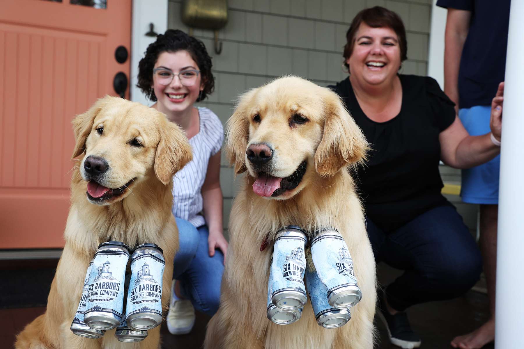 Lisa Fascilla, with children Nina and Alex  receive a beer delivery from Karen and Mark Heuwetter and their two dogs Buddy and Barley on May 03, 2020 in Huntington Village, New York.  Mark and Karen Heuwetter own the Six Harbors Brewery and have trained their two Golden Retrievers Buddy and Barley to help them deliver beer to their customers during the coronavirus COVID-19 pandemic.  The dogs are fitted with a four pack of empty beer cans around their necks and meet customers at their doorstep while Mark and Karen carry the beer to deliver behind them.  It has been comforting for the dogs who are enjoying the exercise and meeting people along the way.  The customers love seeing Buddy and Barley and enjoy petting and greeting them to go with their beer delivery. 