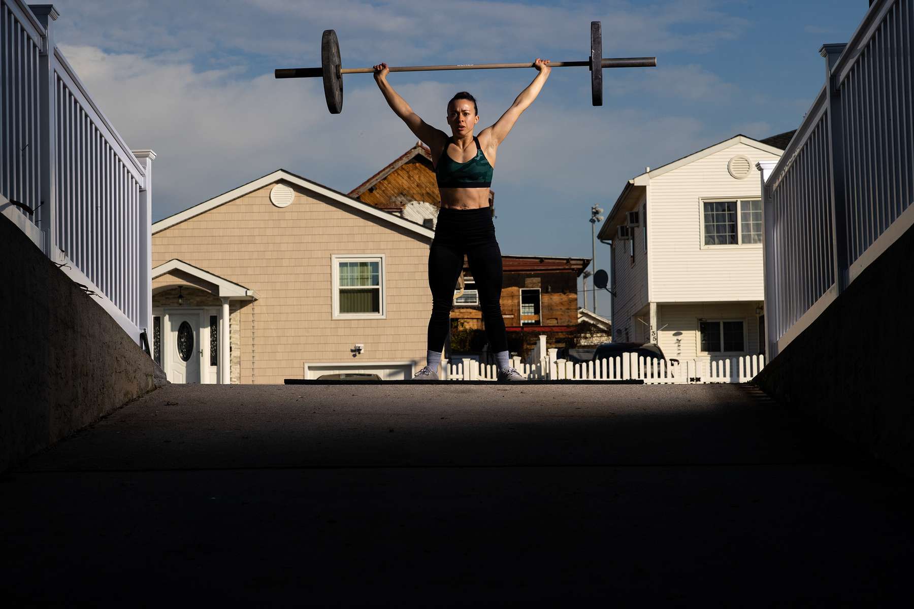 Nicole Guerrero exercises in her driveway with her virtual Fitness Trainer and Husband Dennis Guerrero on November 21st, 2020 in Long Beach, New York.  In March of 2014, Dennis Guerrero and his business partner opened a gym on Long Island. The pair shared a passion for fitness, a dream of creating a local community of like-minded people and a willingness to take a risk. Over the next six years, hundreds of members experienced and embraced a unique environment that fostered a palpable energy, helping athletes of all ages and abilities reach their potential.  The gym became a place to share achievements, work through losses and overcome illness. But like so many other businesses, it seemingly had no way of overcoming the financial impact and ongoing uncertainty of a global pandemic. With the arrival of Covid-19, the gym shut its doors back in March, with no idea when it would reopen. The owners, though, were far from done. They lent out every piece of equipment they owned to the gym’s members, continued to pay their staff and worked to set up outdoor classes in hopes of keeping their membership active and healthy. As the shutdown stretched on, it became clear that the physical gym was closed for good.  They have since reinvented themselves and are now called Life Outside the Box.  Their business model has changed drastically, and all their workouts have gone virtual.  The workouts are conducted by a small group of fitness trainers led by Guerrero.  The members pay a monthly fee and can take live Zoom fitness classes.  They are coached by the virtual trainers in real time.  More and more people have reconstructed their garages, spare rooms, backyards, and basements into home gyms since the COVID-19 pandemic hit the United States.