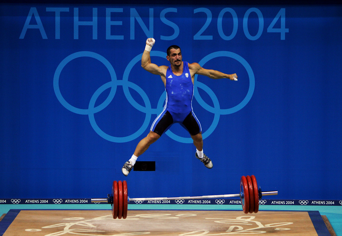 Pyrros Dimas of Greece jumps in the air as he celebrates a successful lift in  the men's 85 kg category weightlifting competition on August 21, 2004 during the Athens 2004 Summer Olympic Games at Nikaia Olympic Weightlifting Hall in Athens, Greece. 