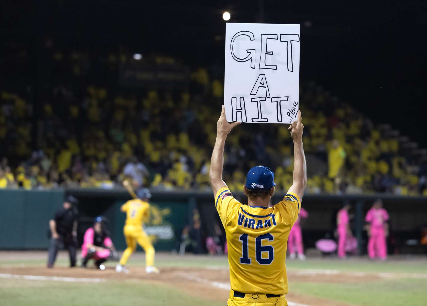 The first base coach of the Savannah Bananas holds a sign during the home opener against the Party Animals at Grayson Stadium on February 25, 2023 in Savannah, Georgia.