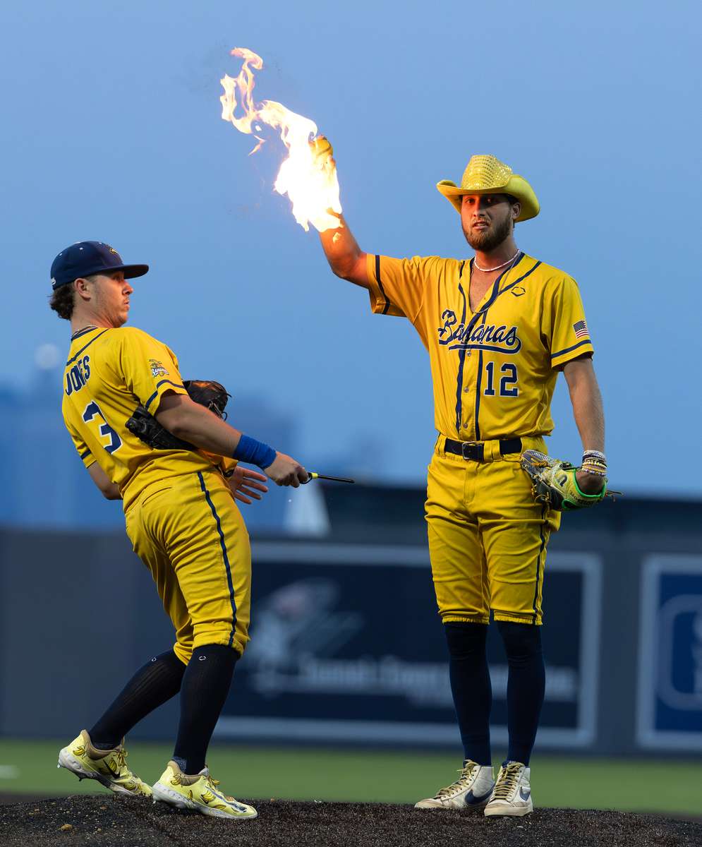 Kyle Luigs #12 of the Savannah Bananas has his ball lit on fire by his teammate Eric Jones Jr. #3 before he pitches it during their game against the Staten Island Ferryhawks at Richmond County Bank Ball Park on August 11, 2023 in New York City. 