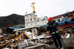 With a boat washed ashore in the background, a member of the Chinese rescue team records video footage at Ofunato, Iwate.  