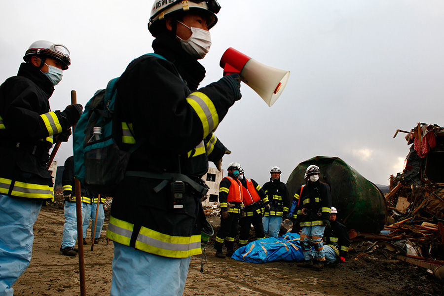 Japanese firefighters along with other search team members recover a body amongst the wreckage in Rikuzentakata, Iwate.