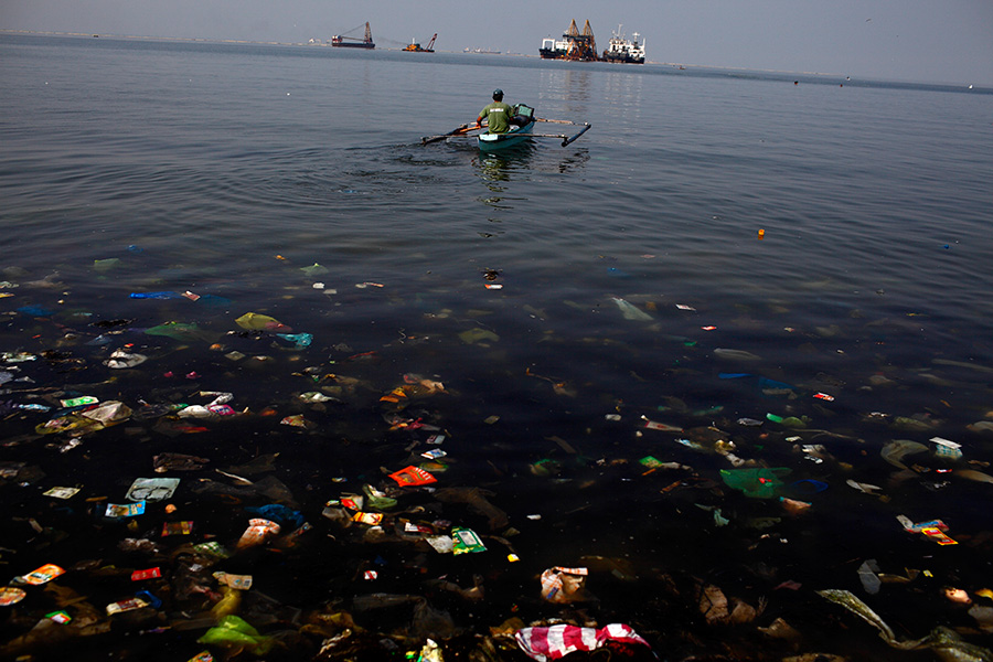 A man paddles a boat through garbage out to the shore in Baseco shanty town in Manila, Philippines.  