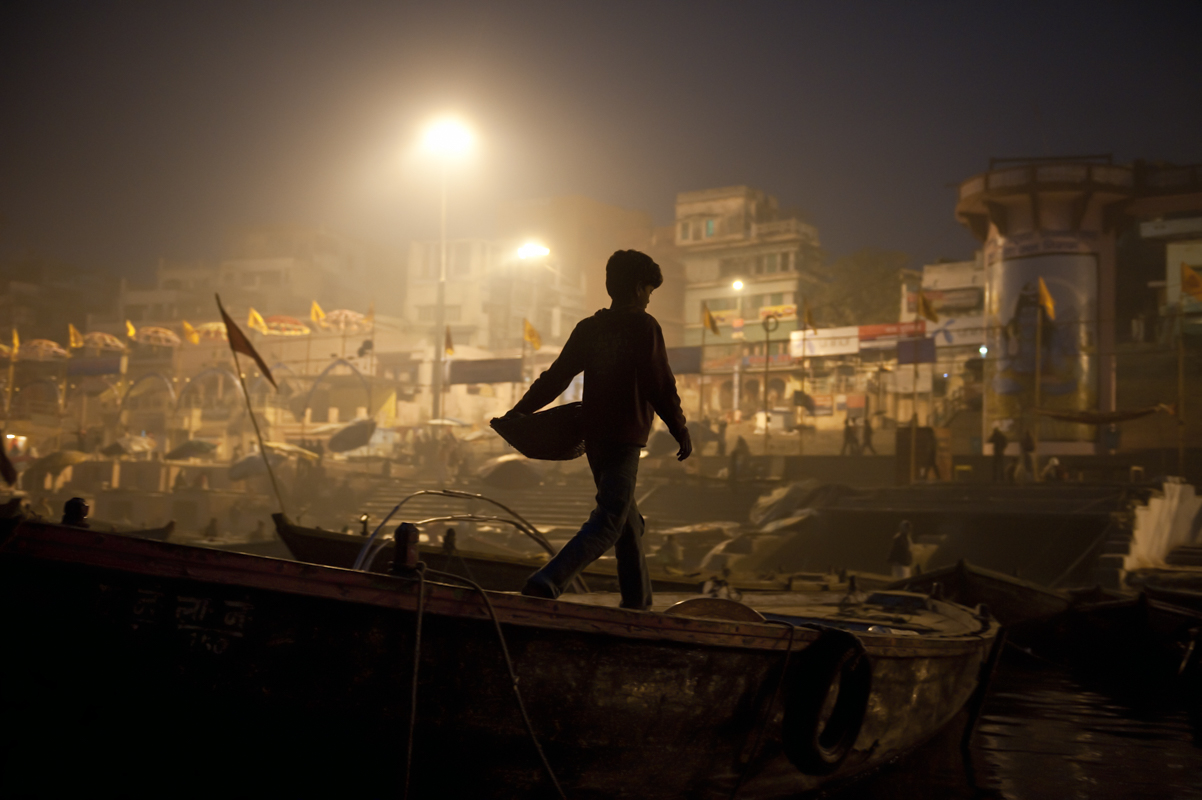 A young souvenir vendor walks among the boats on the Ganges River in Varanasi, India.