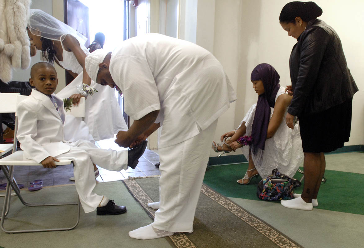 Groom Abdullah Marcus Phelmetto, center, ties his son Amir's shoelaces while bride Aiesha Wilkes-Phelmetto, second from right, puts her shoe on at the conclusion of their wedding ceremony at Masjid Al-Islam.  Though she is Christian, Wilkes-Phelmetto and other non-Muslim women cover their heads while in the mosque.