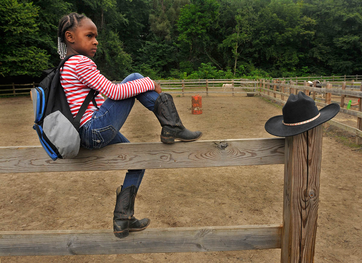 Elaisa Thomas, 9, of Hartford, prepares to watch a horseback riding barrel race in the paddock at Ebony Horsewomen Equestrian Day Camp at Keney Park.  