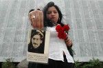 In front of a memorial for those missing, a young woman holds up a photograph of her uncle who went missing during the Pinochet dictatorship.  