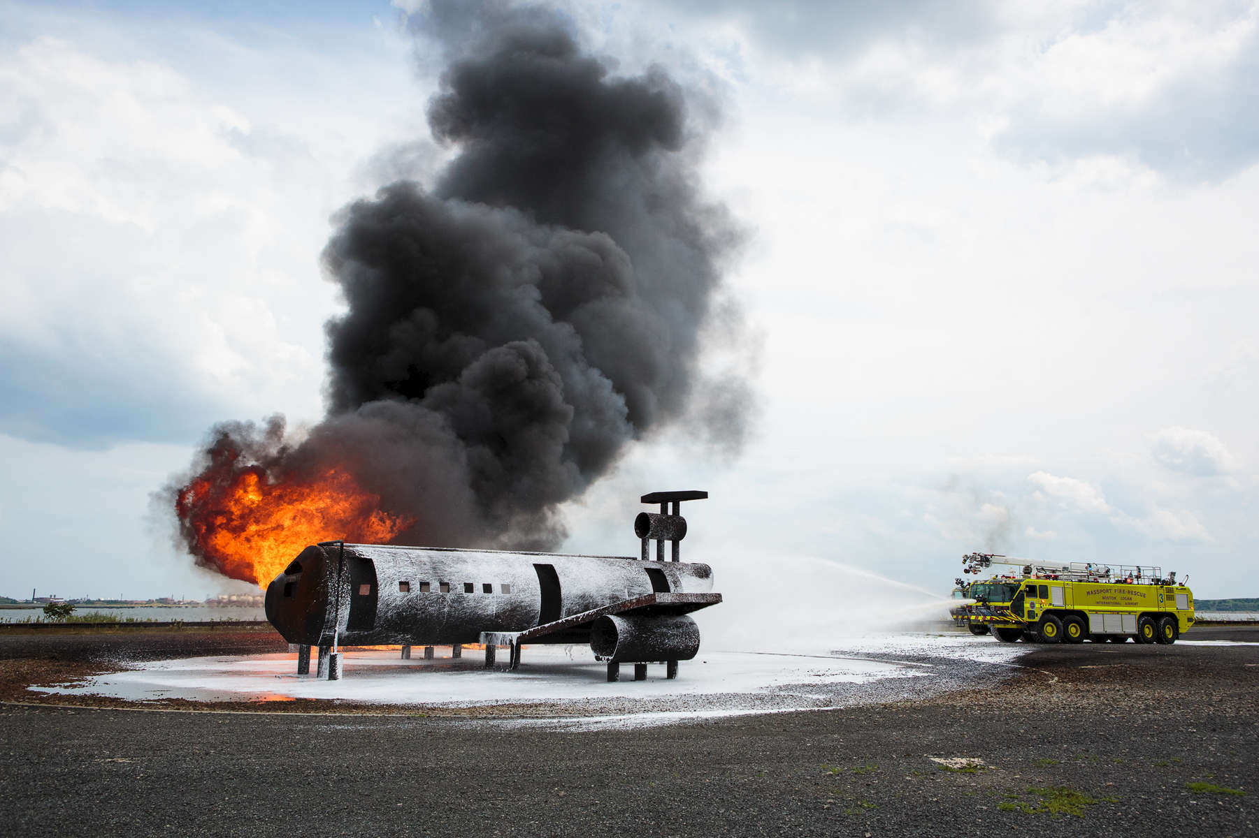 Boston, MA., July 24, 2013: Fire trucks put out a plane fire on a mock plane fuselage during a training session at Boston's Logan Airport. Boston has one of the best airline fighting fighting crews in the nation. Photograph by Evan McGlinn for The New York Times.