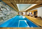 Large swimming pool in private residence with feature stone wall and layered pine ceiling with view to spa area