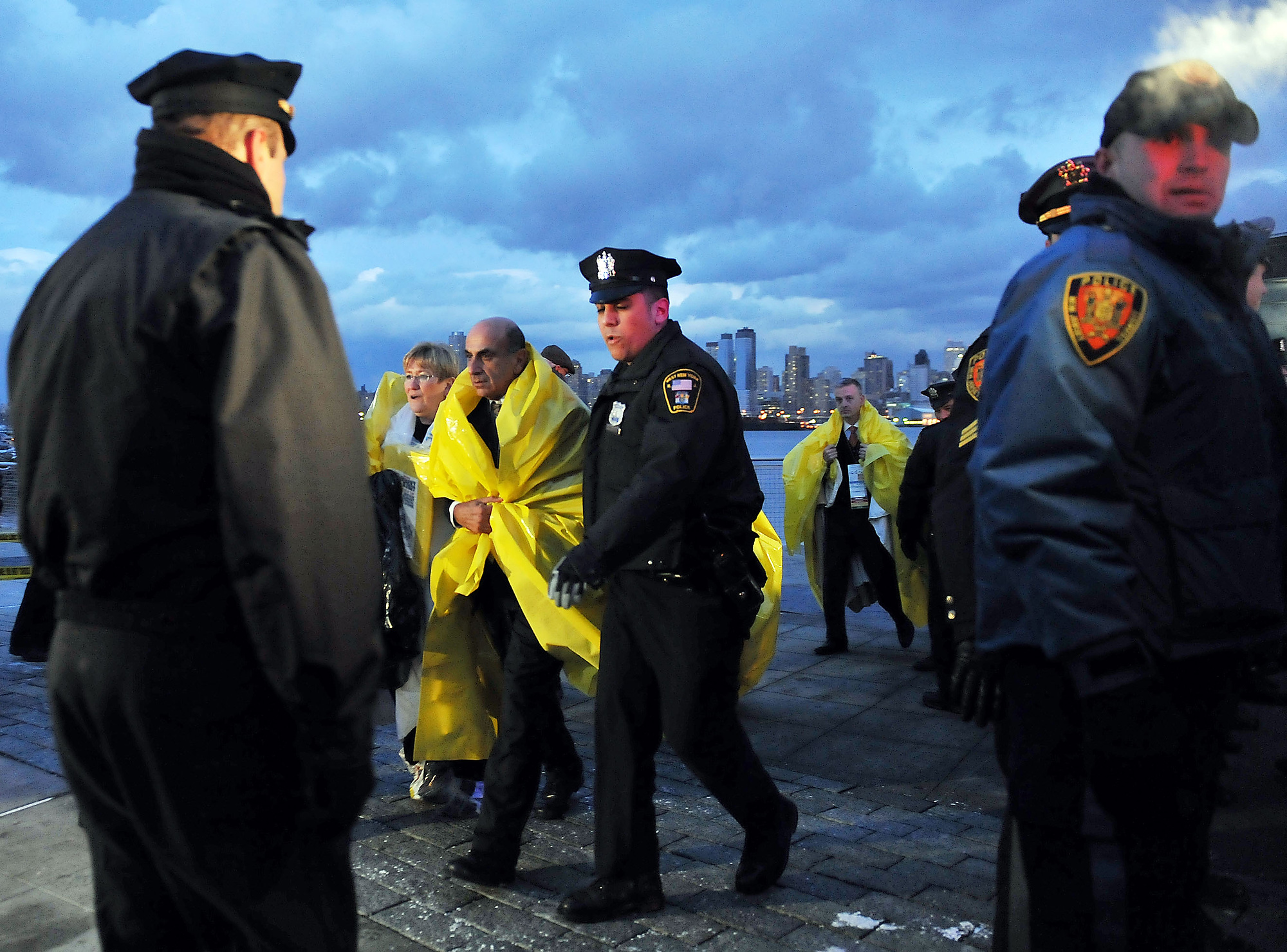 Survivors of the US Airways Flight 1549 bound for Charlotte, N.C.--which made an emergency landing on the Hudson River after both engines failed when the plane struck a flock of geese during takeoff minutes earlier at LaGuardia Airport--are escorted by police from the NY Waterway Port Imperial ferry terminal, to board a bus that will take them to the senior citizen nutrition center to be reunited with their loved ones. (Reena Rose Sibayan | The Jersey Journal)