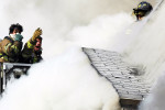 Firefighters reach out to others trapped on the roof of a house on Randolph Avenue while battling a three-alarm fire. The firefighters on the roof were rescued by those on the tower ladder. Four homes were damaged and four people were injured including three firefighters. (Reena Rose Sibayan | The Jersey Journal)