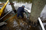 Raul Vervuzco of Eagle Services uses a suction hose to clean oil from atop the Kalamazoo River in a containment area in Augusta nearly 30 miles away from the original ruptured pipeline. 