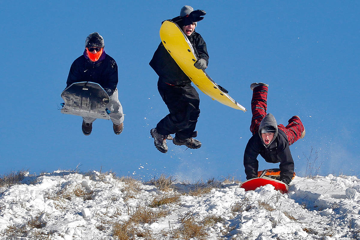 From left Spencer Satchell, 16, Carter Ashley, 14, and Nick Long, 15, jump into the air to gain speed while sledding down a hill at Riverview Farm Park in Newport News Wednesday morning.  