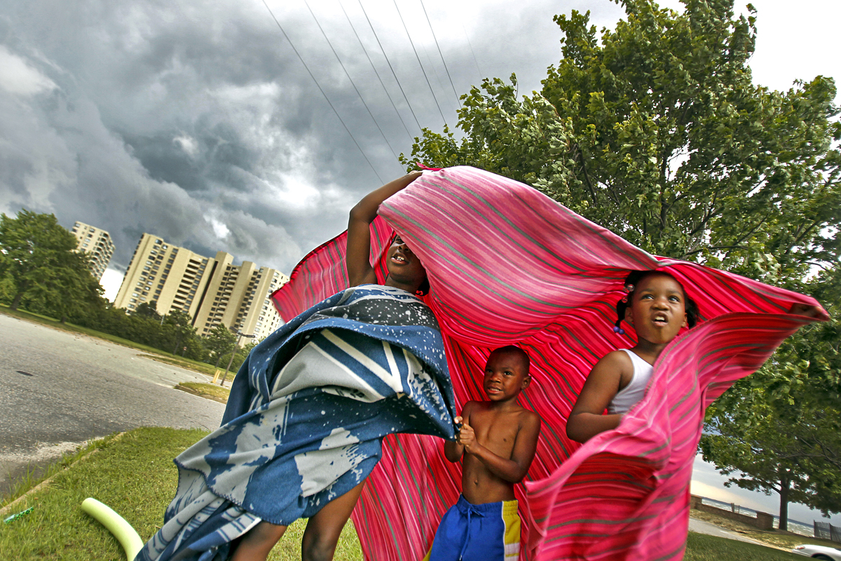 Jacquela Wynn, left, Zyion Jones, center, and Serenity Jones attempt to take cover underneath a blanket as high winds, rain and storm clouds approach Huntington Beach.