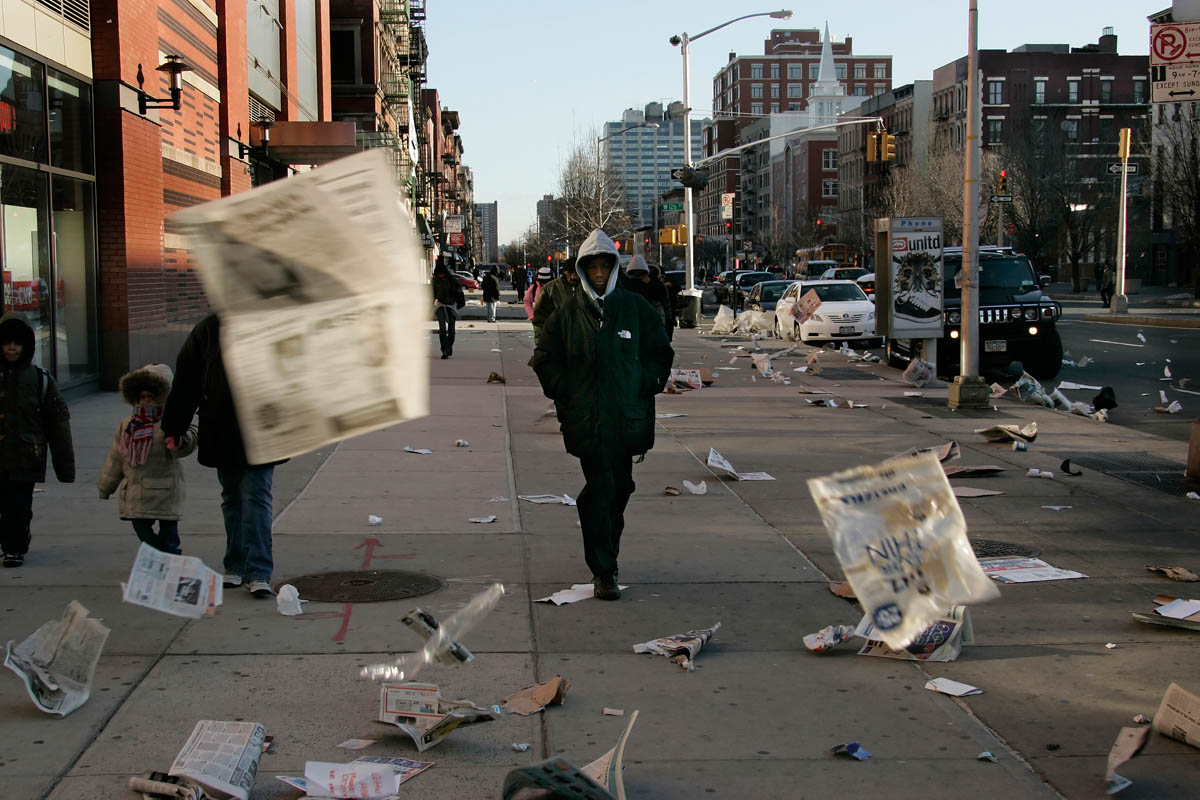 March 2006 - High winds blow loose newspaper pages around 125th near the IRT Subway entrance as some people make their way to work that morning.