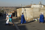 A group of worshippers head home (most church services are over at this time - it was near dusk and there is a little to no electricity in Alexandra Township) from a service. Their garments indicate the congregation or christian association they are a part of. The man in the middle is holding a very beautifully carved staff. The kind one would see in common biblical illustrations. 