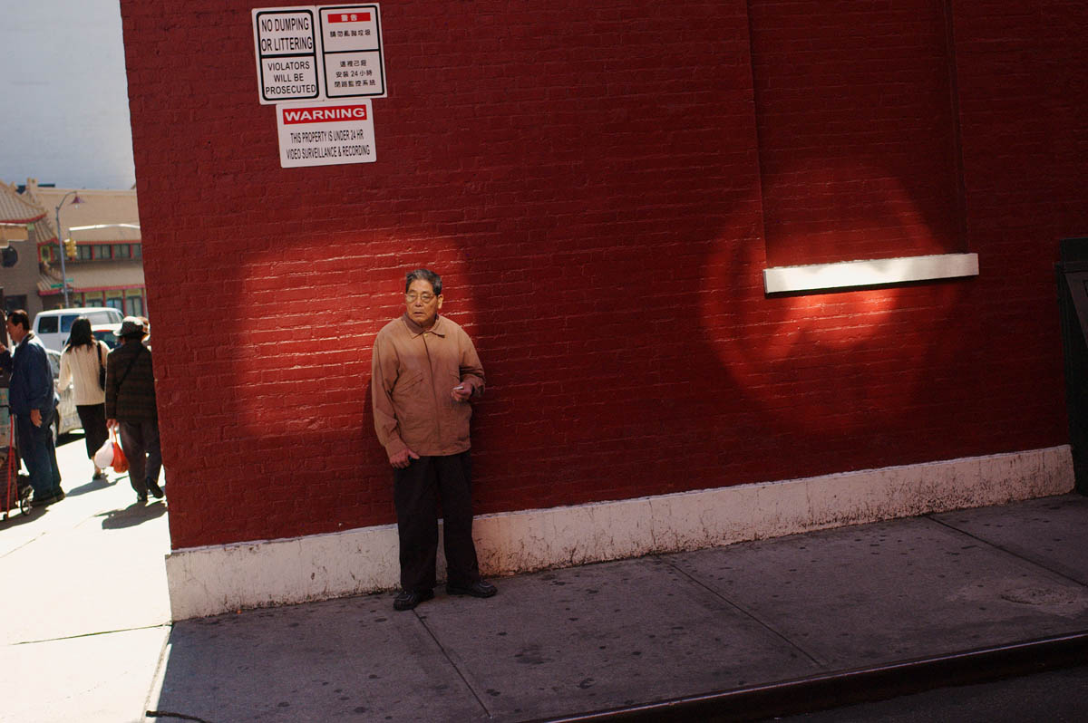 A man smokes a cigarette among shadows and circles of light in Chinatown.