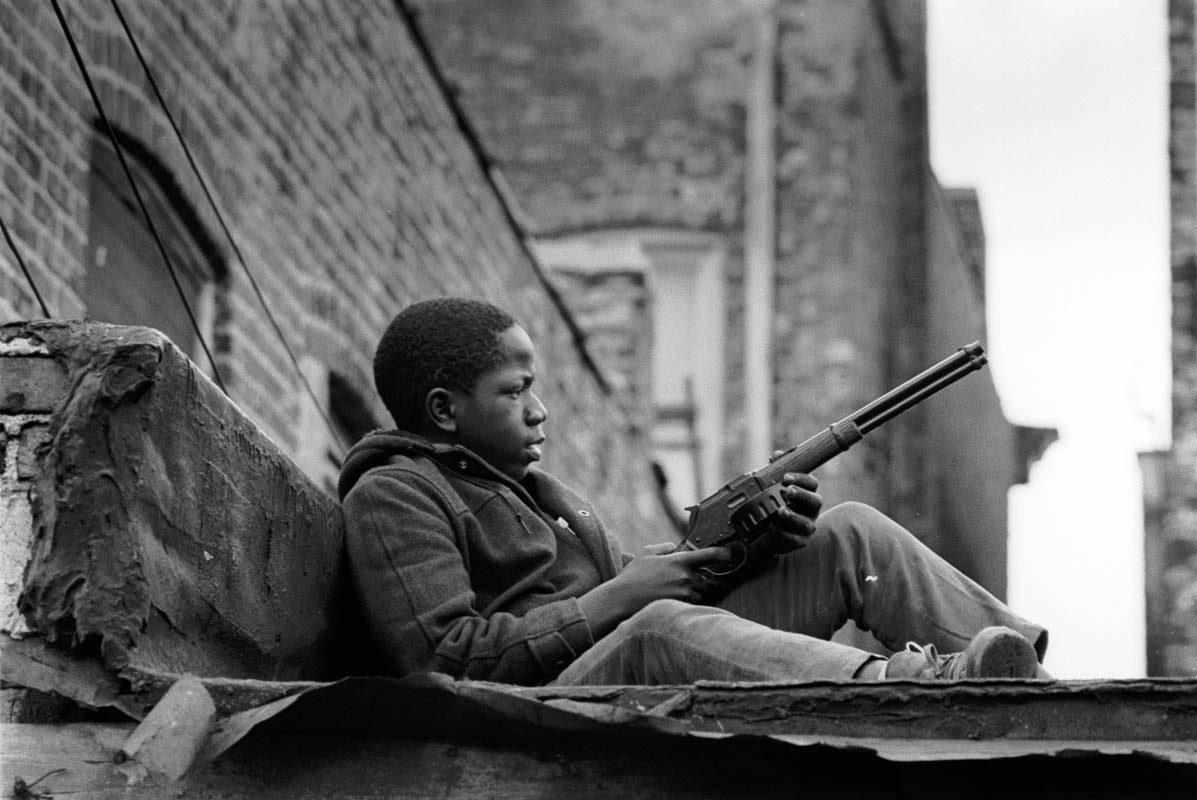 This boy was perched on the roof of a garage behind a tenement building in the Bronzeville neighborhood, holding a toy rifle.