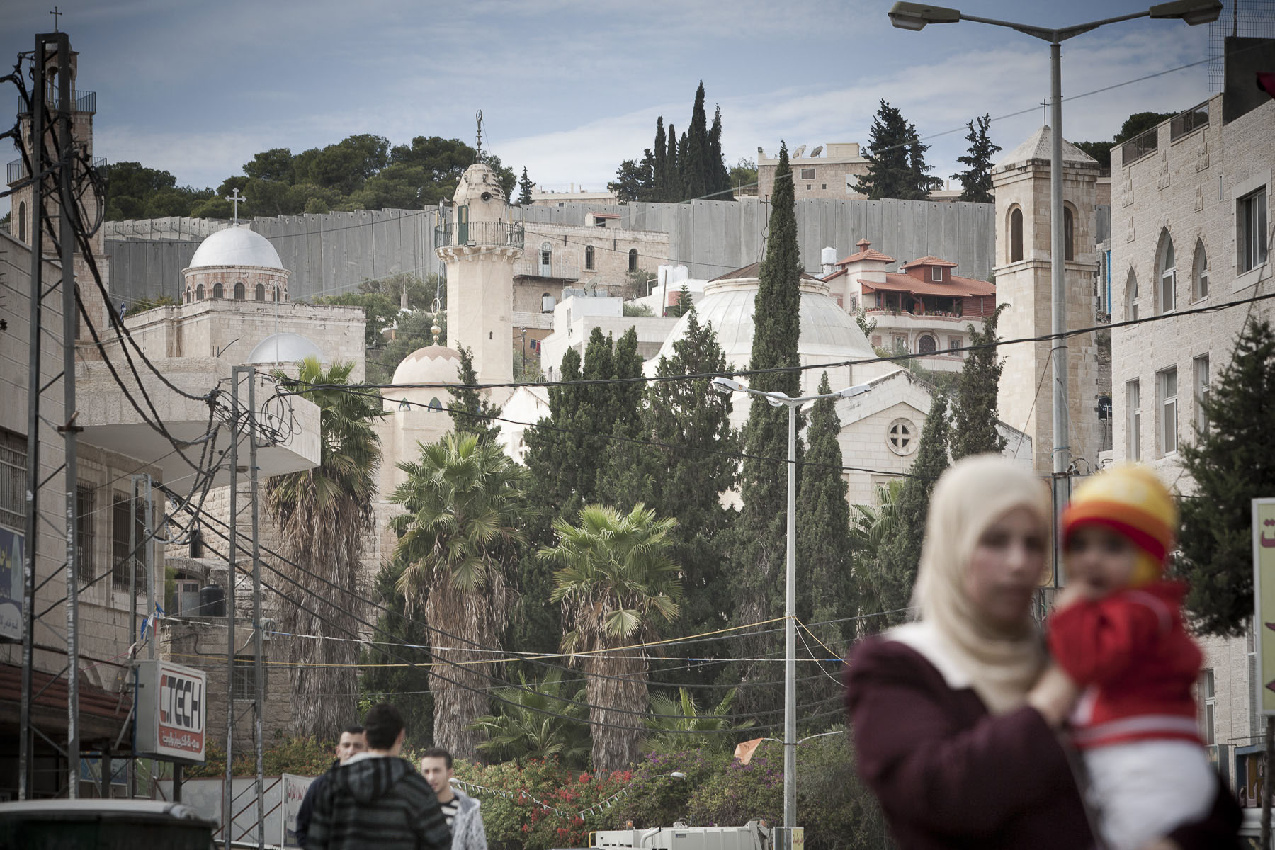 A Palestinian woman with her child. In the background the Tomb of Lazarus and the separation wall in November 2009