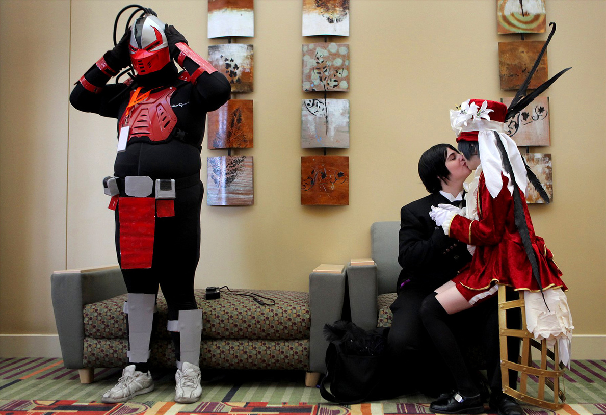 Miles Yagami, 19, of Las Vegas, Nevada gave a kiss to Hollie Green, 20, as George Delorean, left, of Salt Lake City adjusted his helmet during the 6th annual Anime Banzai at the Davis Conference Center in Layton, Utah. 