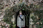 A young woman stands in a doorway surrounded by fall leaves and ivy in France. by Vermont photographer Judd Lamphere