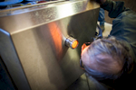 Man peers into a pellet stove while sugaring. By Vermont photographer Monica Donovan 