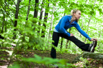 Young woman stretching while running outdoors in forest. by Vermont photographers at Reciprocity Studio, Burlington