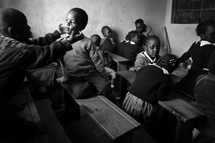 Simon Githui, 4, left, Abdallah Salim, 4, second from left, and other nursery school students play while their teacher, at the front of the room, administers a test to three students at a time. {quote}I can't test the entire class at once because they would just play with and tear or stain the paperwork,{quote} says Cecilia Muringi.