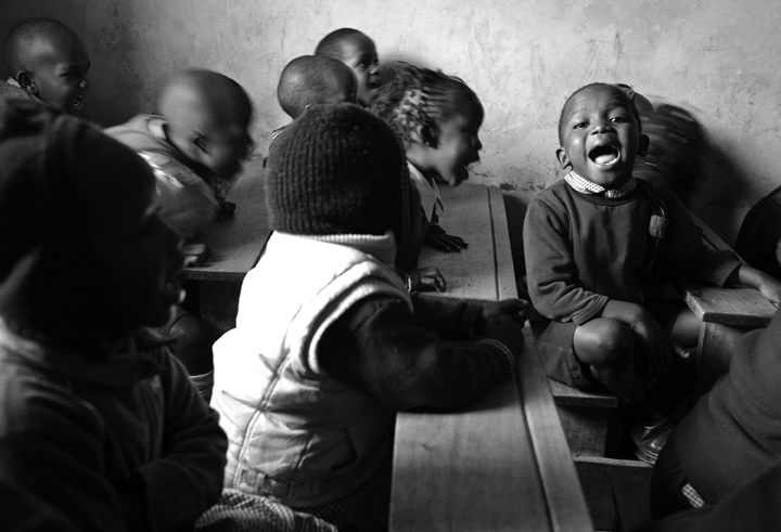 Nursery school students sing along with their teacher who is at the front of the room.