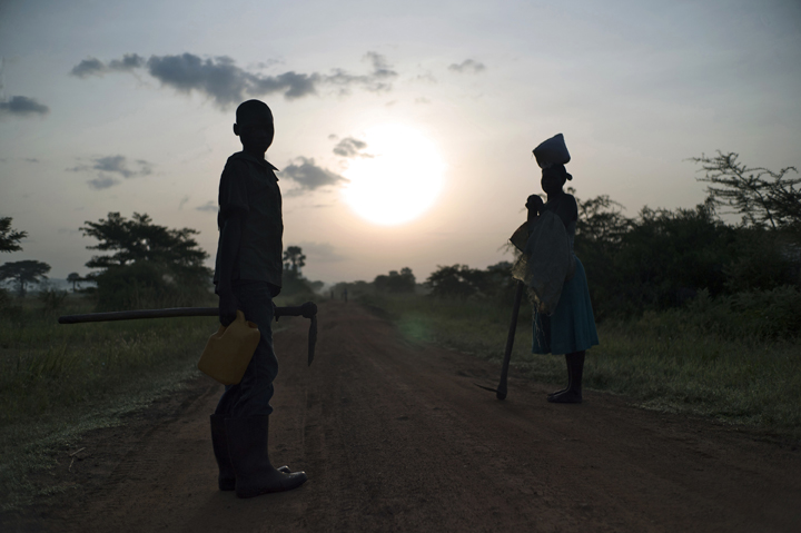 During sunrise Phillips Oluoch, 12, left, who had to stop attending school because his family could not afford school fees, waits with his mother for several village women, as they make their way to work in the field. The hidden cost of schooling is overwhelming in the post-conflict Acholi sub-region. Children constitute an invaluable source of stopgap labour for households re-establishing livelihood strategies. 