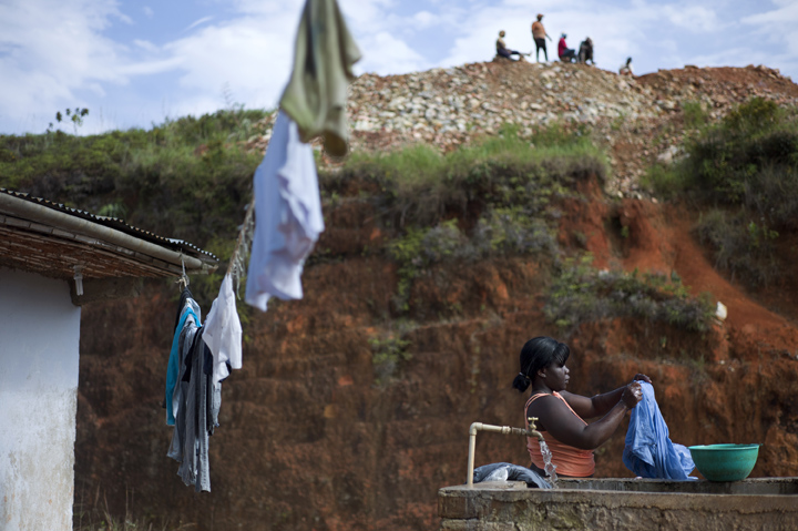 A young woman washes clothes while small-scale gold miners relax overhead during their morning break.