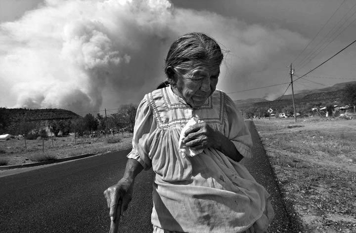 Eleanor Bullock, a White Mountain Apache, walks home as a plume of smoke from the Rodeo-Chediski fires paints the sky. 