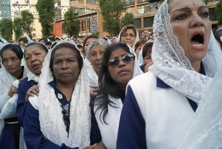 Women dressed in traditional purple capes watch and sing as a procession carrying a painting adorned with the image of Our Lord of Miracles arrives. 