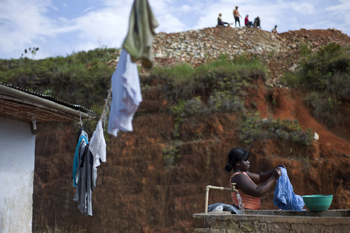 Maria Yuly, 25-years old, the daughter of a miner, washes clothes as several gold miners relax overhead during their morning break.