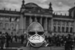 May 16, 2020 - Berlin, Germany:  A man wears a protective mask that reads: Anti Merkel Maske (Anti Merkel mask) and holds a placard that reads: Die die am wenigsten wissen gehorchen am besten (Those who least know obey best) as people gather in front of the Reichstag to protest against lockdown measures and other government policies relating to the novel coronavirus crisis short before police startet to clear the space of demonstrators. Thousands of protesters from a wide spectrum of political creeds, from far left to far right, from the simply disgruntled to conspiracy enthusiasts, are gathering in cities nationwide to protest against government policies and measures many decry as disproportionate and undemocratic. Germany has been easing lockdown measures over recent weeks in an ongoing process. 