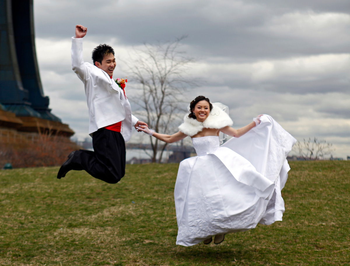 Newlyweds bride Dana Dong, and groom Jeremy Chen jump for joy while having their wedding photos taken in Brooklyn Bridge Park