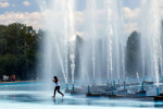 A woman runs through the World's Fair Fountain sprinklers at Flushing Meadow Park