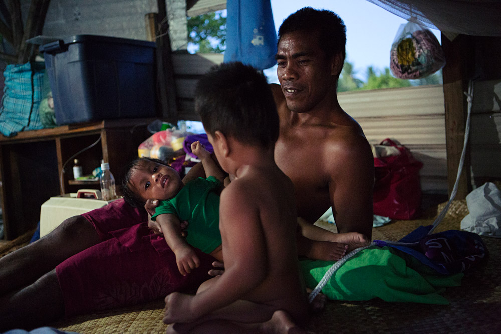 A Father relaxes with his two sons in their home in Ttebikenirkoora Village, Tarawa, an area that has been particularly affected by the rising sea level. THey must now swim home at high tide.