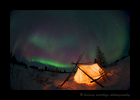A tent is illuminated in the foreground as the northern lights shine in the background in Wapusk National Park, Manitoba, Canada