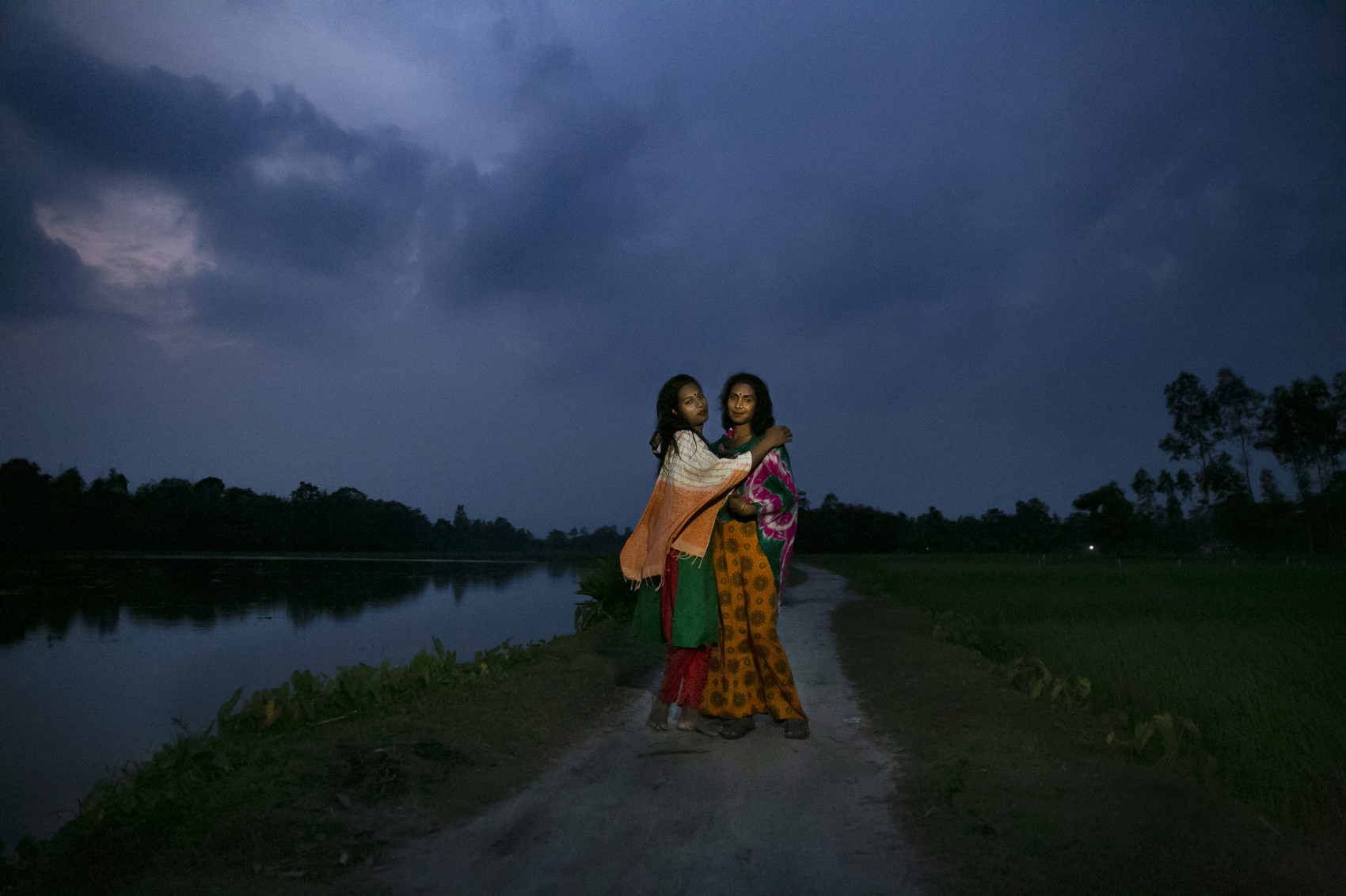 SHERPUR, BANGLADESH - SEPTEMBER 21: Habiba and Rumana post for a photo on the road outside their village on September 21, 2021 in Sherpur, Bangladesh. Rumana was 12 or 13 when she joined the Hijra community. She was born with incomplete genitals and never felt or acted like a boy. She liked to dress like a girl, play with girls, and was always attracted to boys. Rumana met a Hijra group in the market when she was 12 year old and they invited her to join them. {quote}There are two parts of Hijra life; the bad, people bully and hate us. But the positive is that we life together, eat together, have community.{quote} Habiba says {quote}I am also a human being, I have a right to live life as a Hijra and I should not be deprived of that.{quote} She was always bullied in school for acting feminine so she dropped out in class 6. She met some Hijras in a market and joined them when she was very young. In South Asia, “hijras” are identified as a category of people who are assigned as male at birth but develop a feminine gender identity. They are generally outcasted from mainstream society, and have no other way of earning money other than harassing and extorting people for money. A new government initiative aims to change that. Recently, 40 Hijra were given homes, grants, loans, livestock, and livelihood training in an effort to make them self sufficient. (Photo by Allison Joyce/Getty Images)