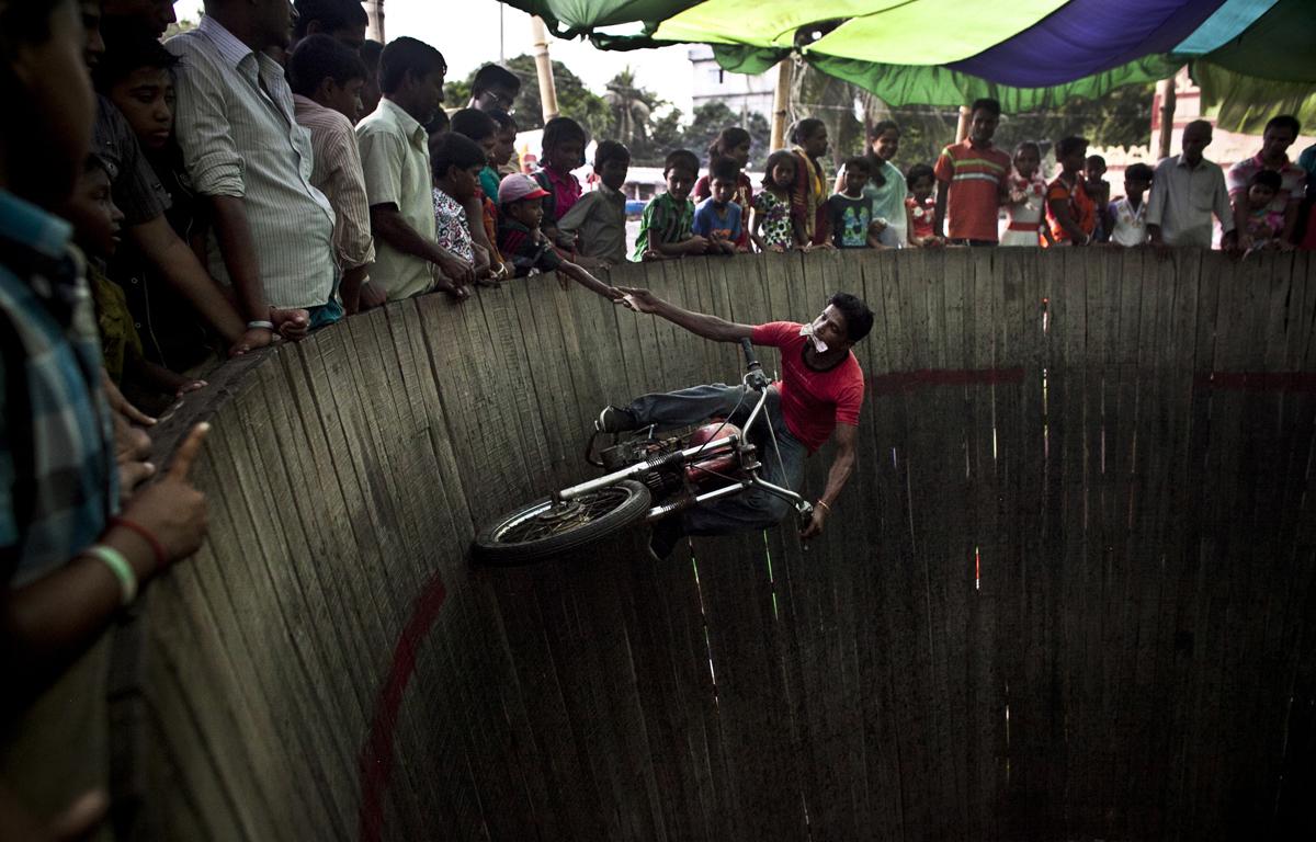 A man collects tips the as he rides a motorcycle  at a circus in Dhamrai, Bangladesh. 