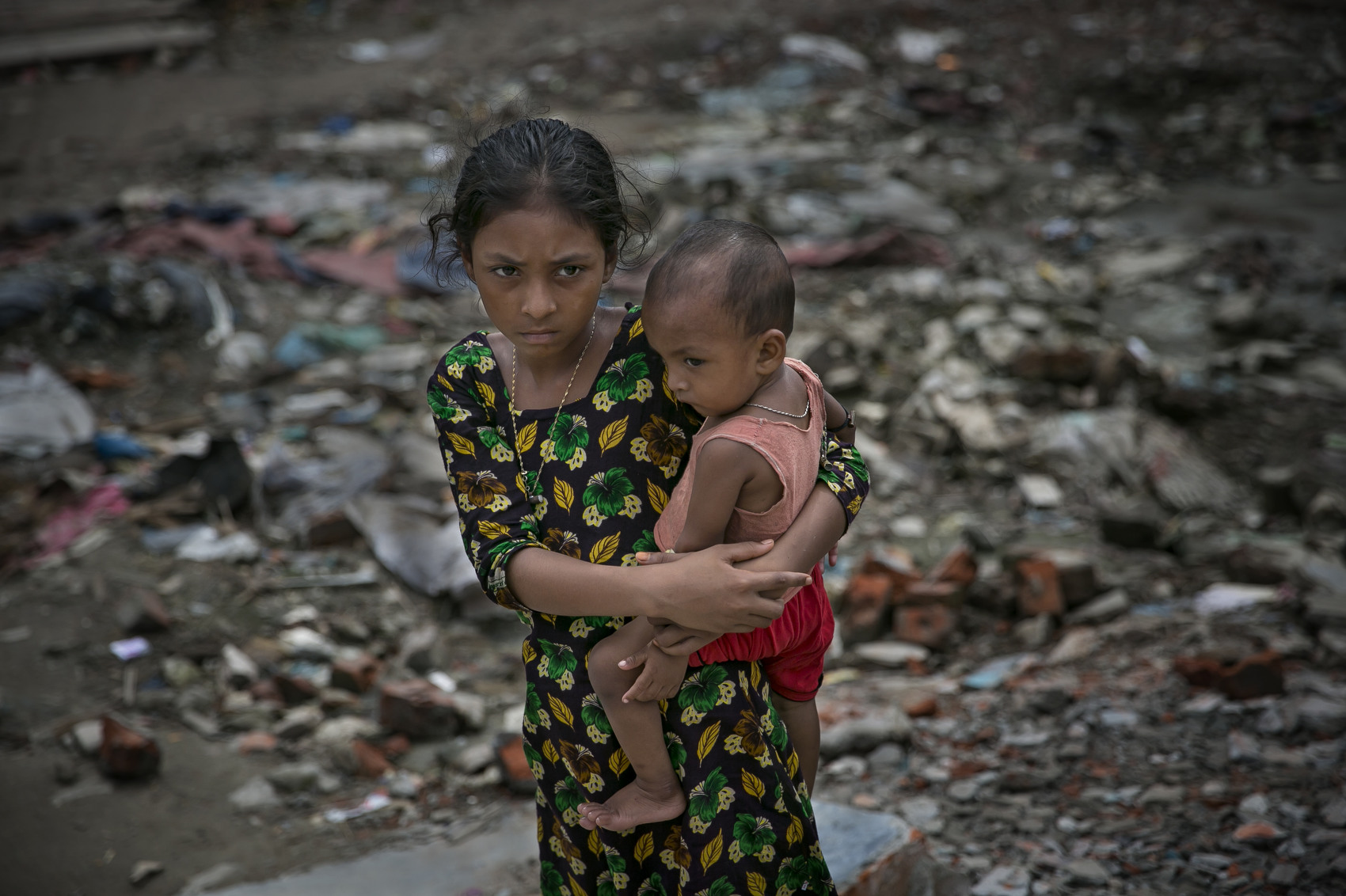 DHAKA, BANGLADESH - JUNE 10:  A girl holds a baby next to a polluted canal that leads to the Buriganga river in Shyampur June 10, 2018 in Dhaka, Bangladesh. Bangladesh has been reportedly ranked 10th out of the top 20 plastic polluter in the world with the Buriganga river known as one of the most polluted rivers in the country due to rampant dumping of industrial and human waste. Like many developing countries, Bangladesh lacks the infrastructure to effectively manage their waste which causes problems in keeping the waters safe for human and aquatic lives while dozens of tanneries on the banks of the river contribute industrial waste into the ground water. As June 5 was marked by the United Nations as World Environment Day, Buriganga symbolizes the general state of many rivers in Bangladesh, with the growing levels of pollutants and plastic waste consuming up all oxygen in the river and affecting our seafood while fishes consume bits of plastic which mimics their natural food sources and eventually lands on our dinner table. (Photo by Allison Joyce/Getty Images)