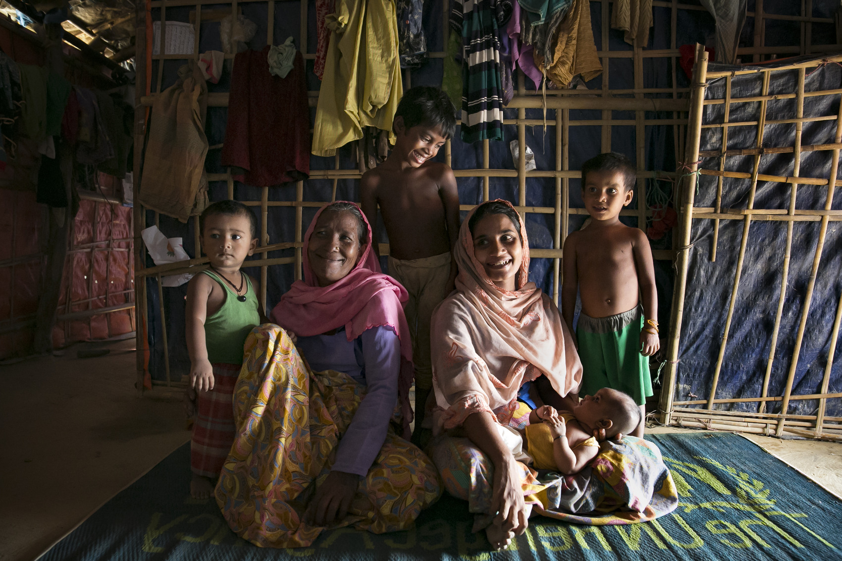 Mother Rohana Begum (25) (center in light pink scarf) baby Khotija (2.5 months), grandmother Toslima (56) (center in dark pink scarf), siblings Mohammed Haque (3), Asmara Bibi (6) and Rohara (7) pose for a photo  September 30, 2018 in the Rohingya refugee camp in Cox's Bazar, Bangladesh. Rohana was brought to the PHCC when she started hemorrhaging immediately after childbirth. When she was stabilised, the PHCC team put her in an ambulance and took her to a hospital, where she received emergency treatment. She made a full recovery. Now, Rohana and Khotija are doing well. They have been back to the PHCC several times for checkups, and Rohana is very happy with the care they have received. Rohana thinks she would have died if it had not been for Save the Children. They now tell other Rohingya women to give birth in the maternity ward at the PHCC, because it is safe and they can receive emergency treatment if needed. 