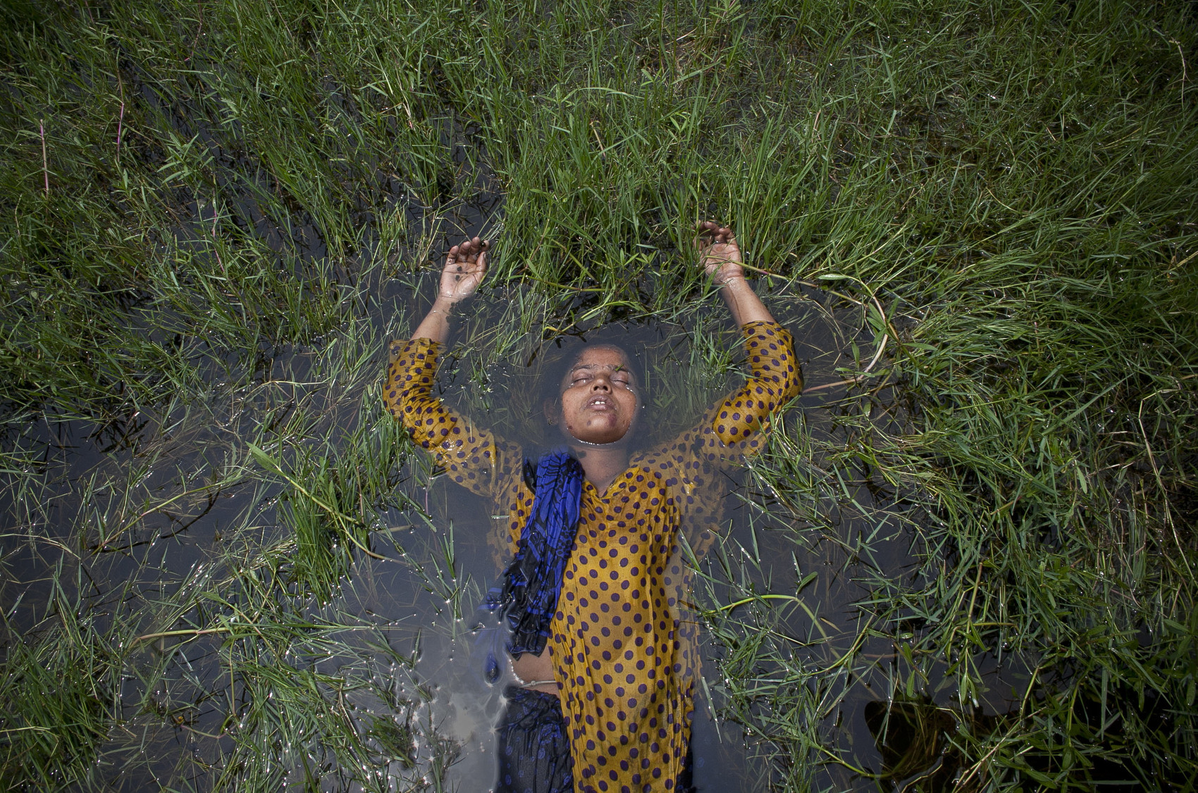 35 year old patient Barvine Akhter lies in a rice paddy outside the intake center of Pabna Mental Hospital in Pabna, Bangladesh. Mental health in Bangladesh is largely neglected and under financed, and the stigma of mental health is huge. In rural areas there are few doctors and families generally take the patient to a traditional healer first, who usually tries to exorcize the Jinn (spirits) with holy water and versus from the Koran. Families who have a mentally ill family member sometimes tie them up out of desperation and lack of education and options. There is only one government run mental hospital with 500 beds in the entire country. Less than 0.5% of government health budget is spent for mental health. 