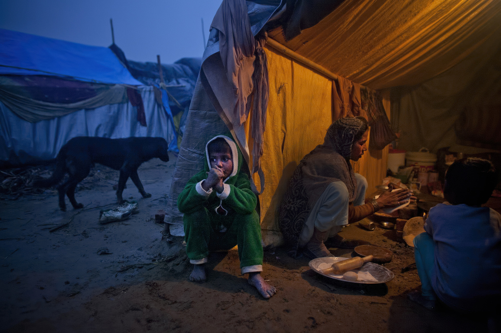 A child sits outside his tent while his mother cooks in the Malakpur relief camp in the Shamli district of Uttar Pradesh, India. Riots between Muslims and Jat Hindus broke out at the end of August and lasted until the beginning of September, 2013. More than 55 people were killed, hundreds were injured, at least 6 women were gang raped, and almost 50,000 people fled to relief camps in the immediate aftermath. The cold winter has led to the death of over 34 children in the relief camps. (Photo by Getty Images/Getty Images)