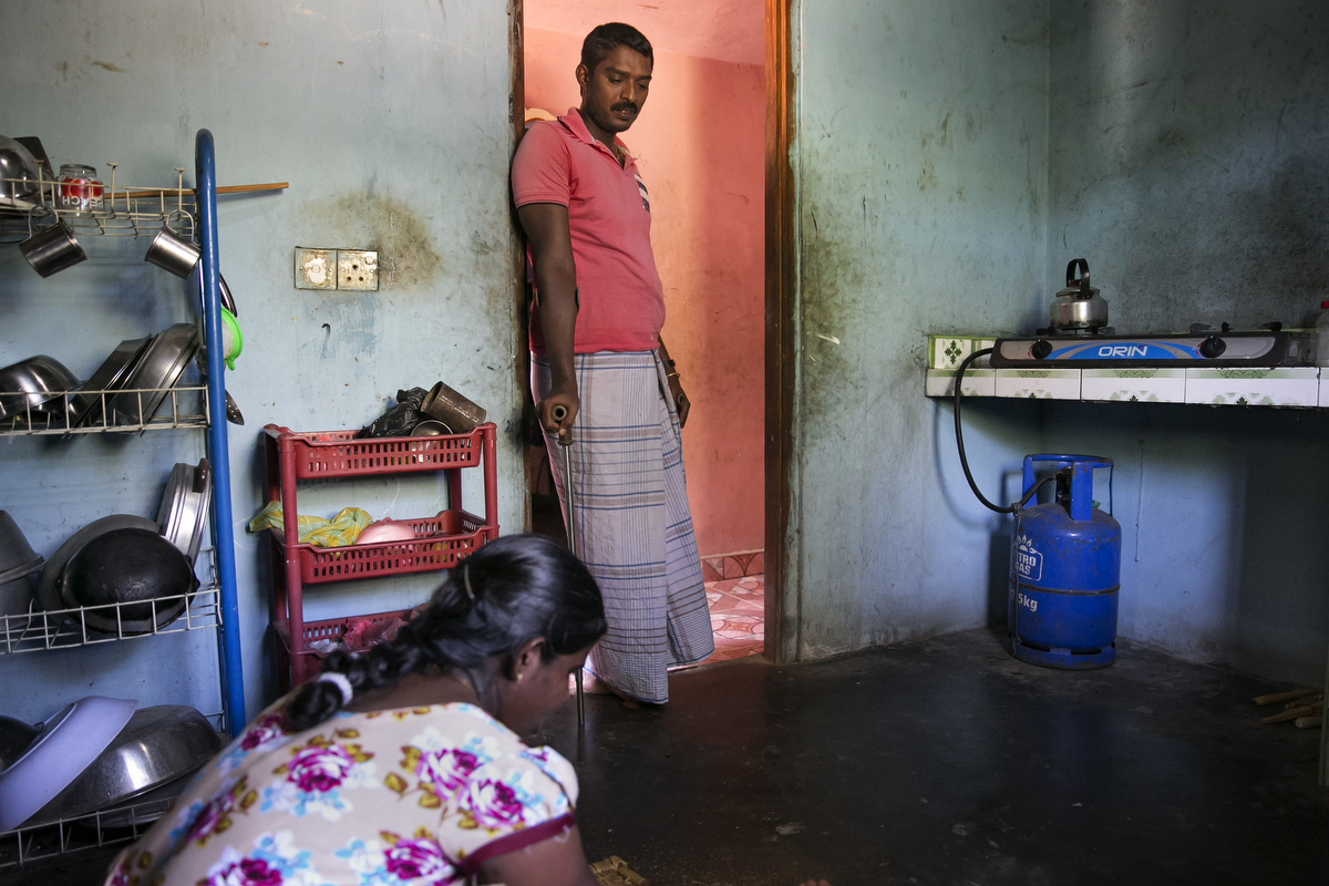 Inthira Piriyatharsini talks to her husband, Ludes Nixon, while cooking for her family in her home after her shift working to clear mines in Muhamalai, one of the biggest minefields in the world,  in Killinochi, Sri Lanka. Inthira Piriyatharsini and her family were displaced in 2009 when the Sri Lankan military shelled their village. Her husband, Ludes Nixon, was hit and lost his right leg during the attack. After a year they were able to move back to their village with their two children. In 2012 Inthira joined the HALO Trust as a de-miner. {quote}I was nervous the first day, and the first time I found a grenade, but I was affected by the war so doing this work is very satisfying for me. I always think that it's just because of my work that people get to come back and live in their homes again{quote} Inthira says. 